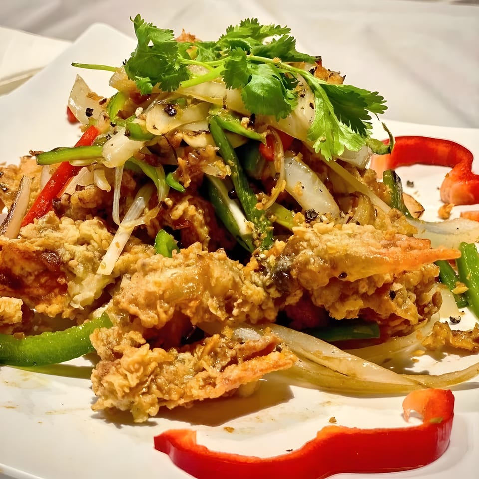 Crispy fried seafood topped with cilantro, onions, peppers, and green beans on a white plate.