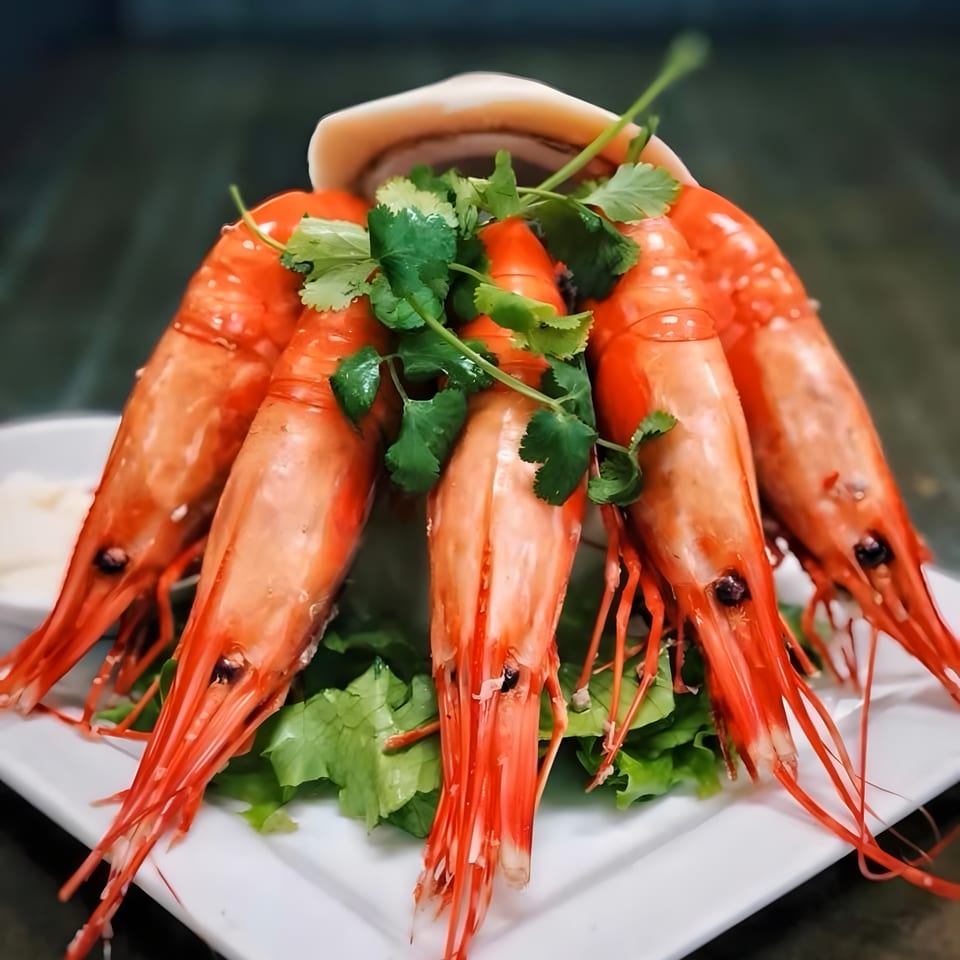 Boiled red shrimp with cilantro and lettuce on a white plate, with a dark background.