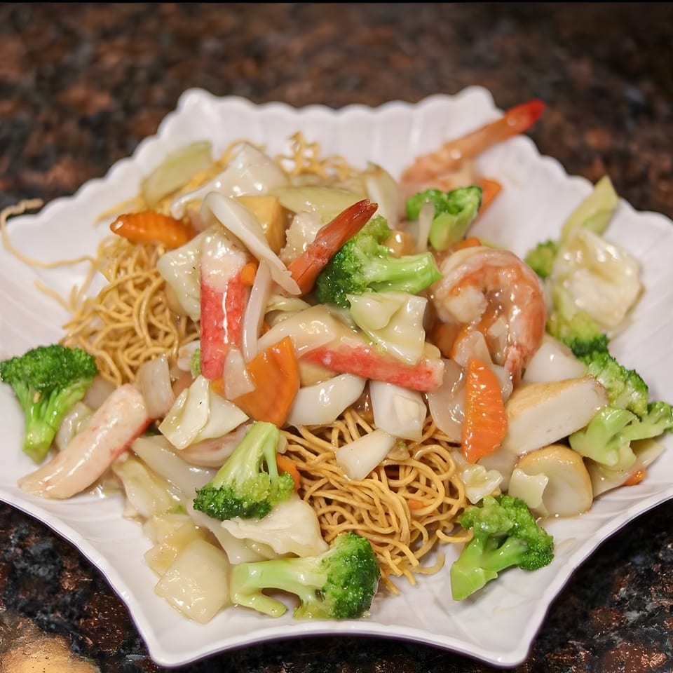 Crispy noodles topped with shrimp, crab, broccoli, carrots, and other vegetables in a white sauce.