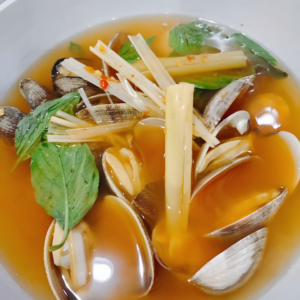 Clam soup with bamboo shoots, basil, and chili flakes in a white bowl.