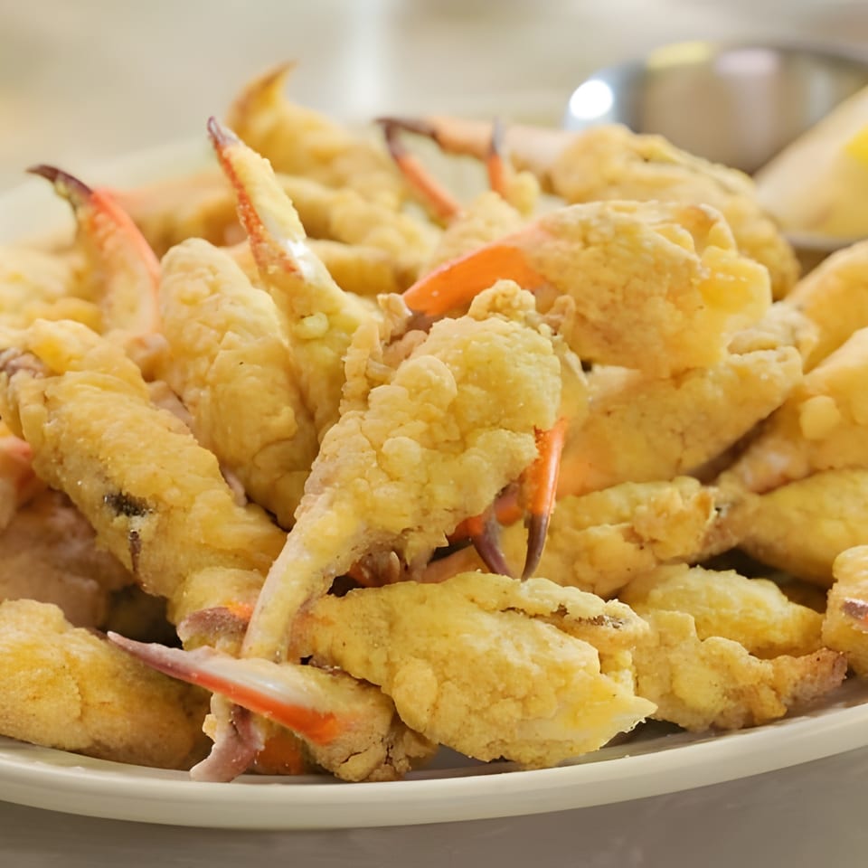 A plate of golden-fried crab claws with a lemon wedge and a metal cup in the background.