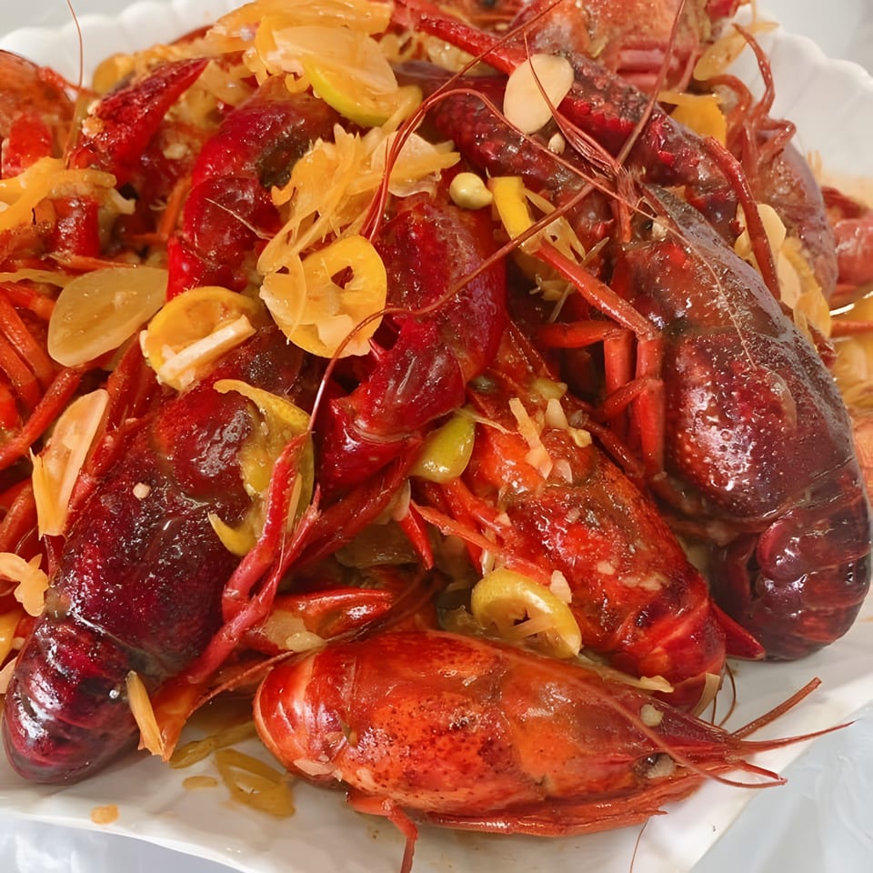A white platter piled high with vibrant red crawfish, garnished with sliced garlic and citrus.