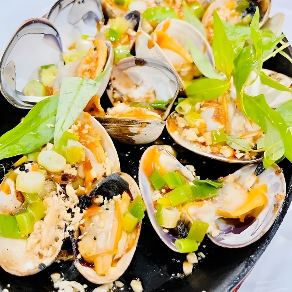 Steamed clams in shells, garnished with green onions, herbs, and a savory sauce.