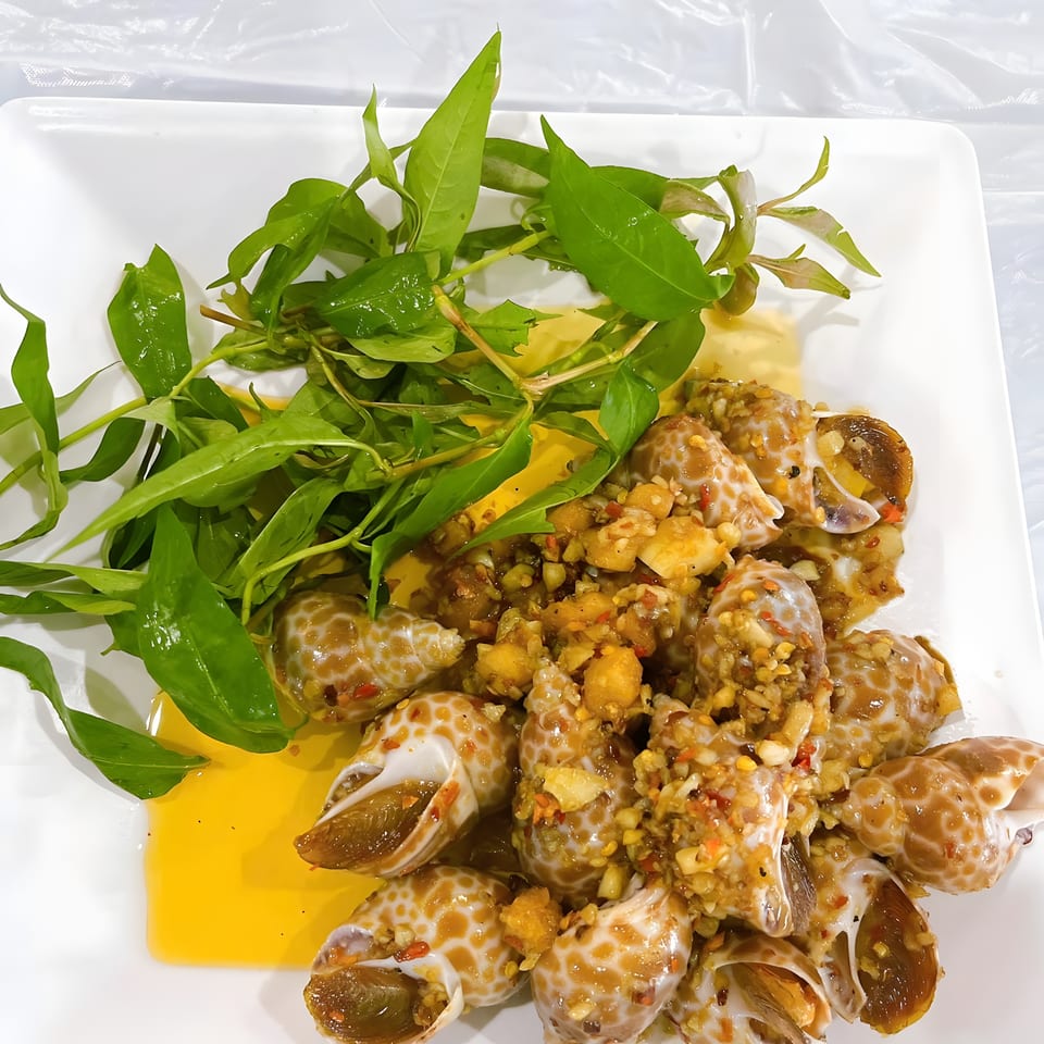 Plate of snails with garlic, chili, and herbs, served with a yellow sauce.
