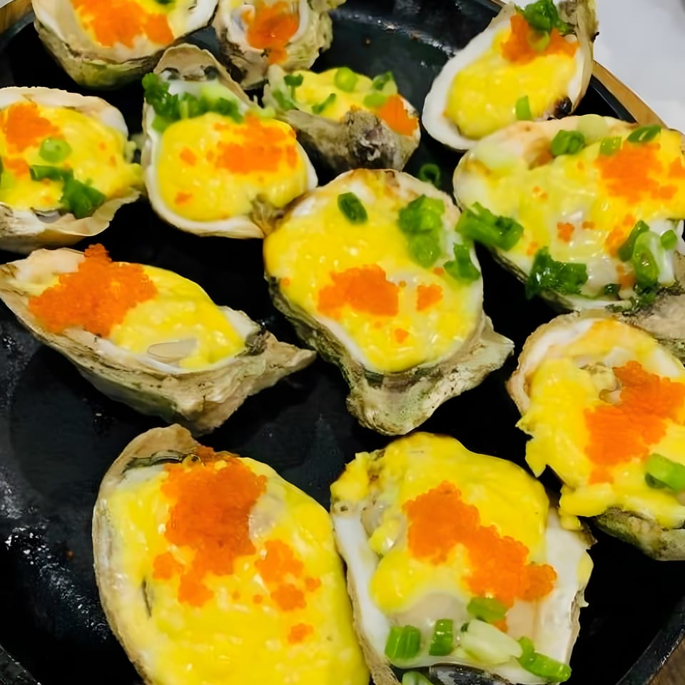 A black platter filled with baked oysters topped with yellow sauce, orange roe, and green onions.