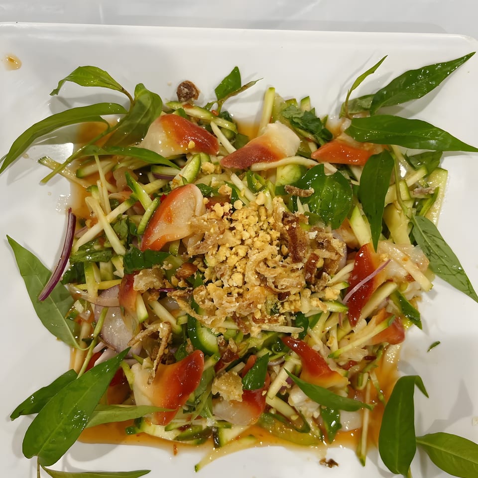 A vibrant Vietnamese mango salad with clams, herbs, and crispy fried shallots on a white rectangular plate.