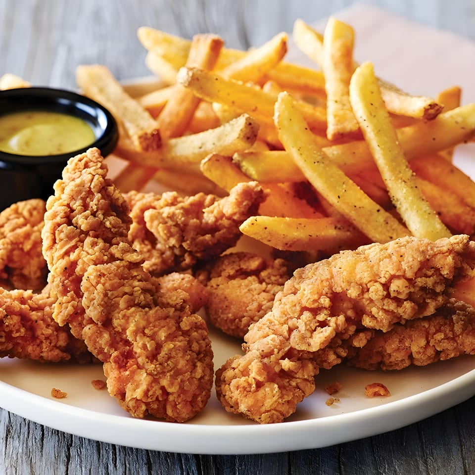 Plate of crispy fried chicken tenders and golden French fries with a small cup of dipping sauce.
