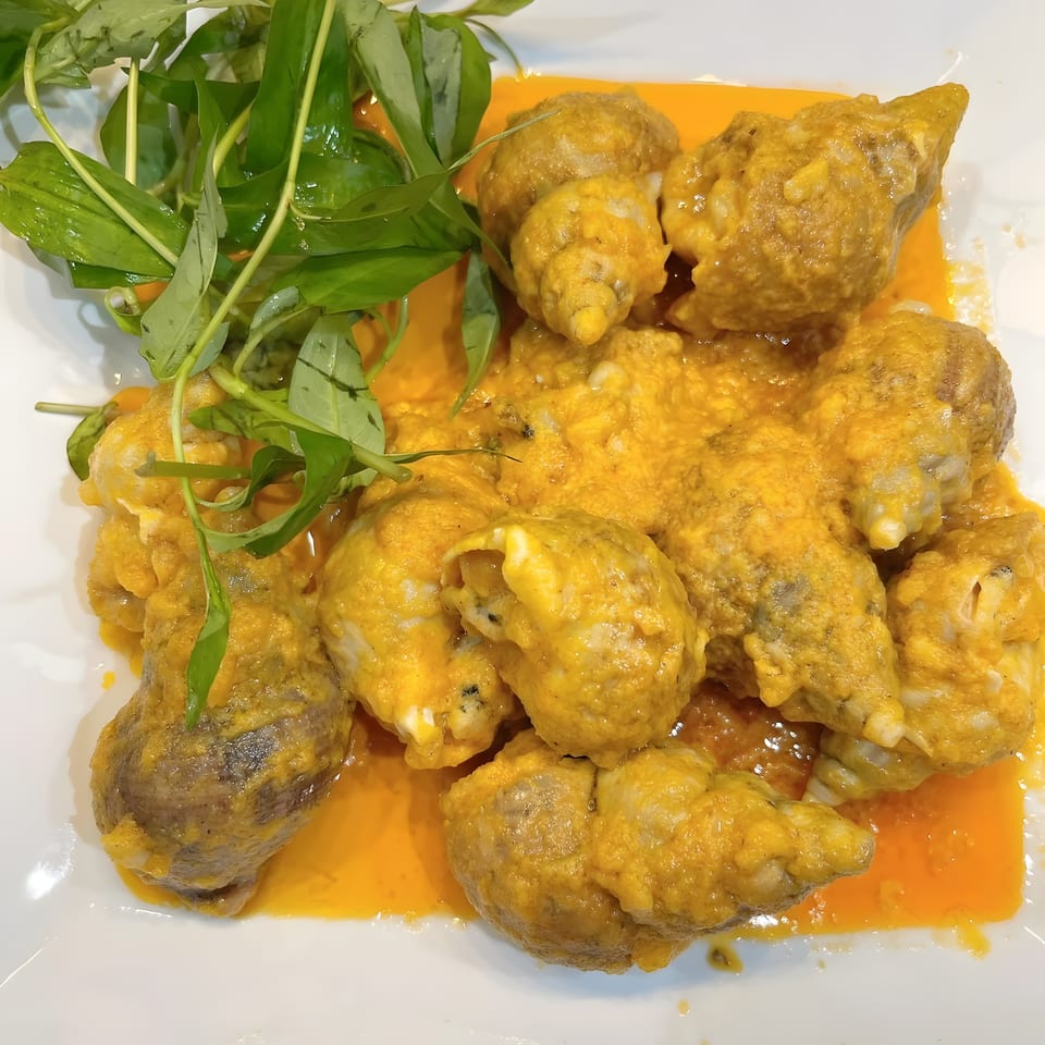 Snails in a rich yellow curry sauce, garnished with fresh green herbs on a white plate.