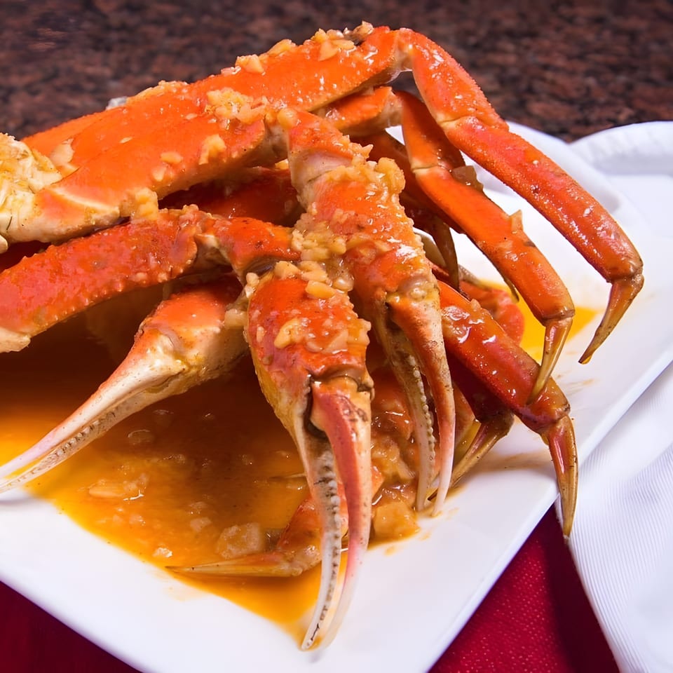 A white rectangular plate holds several bright orange crab legs covered in a savory sauce.