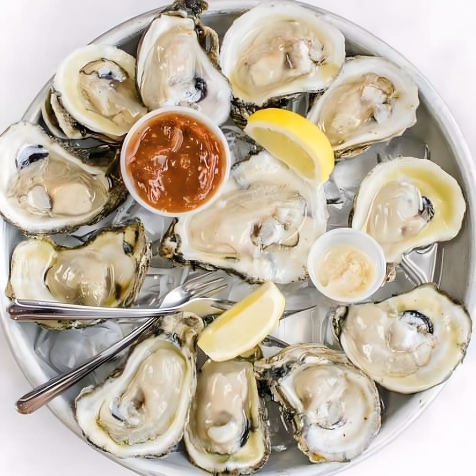 A dozen fresh oysters on the half shell, served on ice with cocktail sauce, horseradish, and lemon wedges.